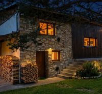 Nachtansicht eines Steinhauses in Dobrá Voda mit Holzlager und Gartenbeleuchtung.