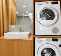 Badezimmer mit Trockner und Waschmaschine in einer 3-Zimmer-Wohnung, Holzelemente und Waschbecken.