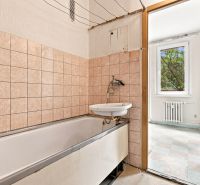 Badezimmer mit Badewanne und Waschbecken, das in einen hellen Raum in einer 2-Zimmer-Wohnung führt.