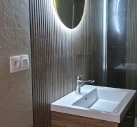 Badezimmer in einem Einfamilienhaus mit beleuchtetem Spiegel und Waschbecken auf einem Schrank mit Holzdekor.