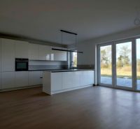 Eine Küche in einem Einfamilienhaus mit einem Boden in Holzoptik und großen Fenstern.