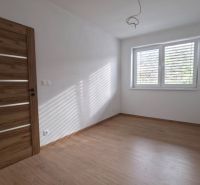 Ein Zimmer mit einem Boden in Holzoptik, weißen Wänden und einem großen Fenster, Einfamilienhaus.