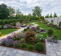 Der Garten des Einfamilienhauses in Hôrka nad Váhom mit gepflegten Beeten, einem Gehweg und einer Außensitzgelegenheit.