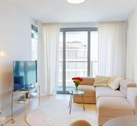 Wohnzimmer in einer 2-Zimmer-Wohnung mit einem bequemen Sofa, einem Fernseher und großen Fenstern.