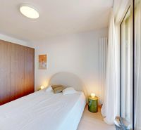 Schlafzimmer mit weißem Bett, großem Schrank und Holzboden in einer 2-Zimmer-Wohnung.