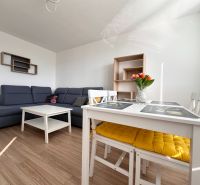 Wohnzimmer mit Ecksofa, weißem Tisch und Boden mit Holzdekor in einer 3-Zimmer-Wohnung.