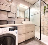 Badezimmer mit Waschmaschine in einer 3-Zimmer-Wohnung; moderne Regale, Duschkabine mit dekorativem Glas.