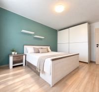 Schlafzimmer in einer 3-Zimmer-Wohnung mit Bett, Nachttisch und Boden mit Holzdekor.