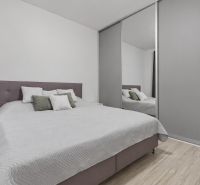 Schlafzimmer mit großem Bett, Einbauschrank und Holzboden in einer Zweizimmerwohnung.
