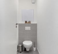 Ein schmales WC mit weißen Wänden und grauen Fliesen in einer Zweizimmerwohnung.