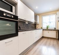 Küche in einer 3-Zimmer-Wohnung mit weißen Schränken und einem Boden in Holzoptik.