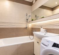 Badezimmer mit Badewanne und Waschbecken in einer 3-Zimmer-Wohnung mit Spiegel und Waschmaschine.
