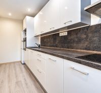 Eine Küche in einer 3-Zimmer-Wohnung mit weißen Möbeln und einem Boden in Holzoptik.