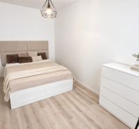 Ein Zimmer in einer 2-Zimmer-Wohnung mit einem Bett, einer Kommode und einem Boden mit Holzdekor.