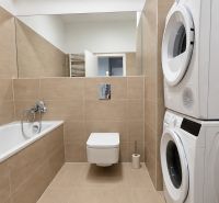 Badezimmer einer 2-Zimmer-Wohnung mit Dusche, Waschmaschine, Trockner und beigen Fliesen.