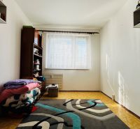 Ein einfaches Zimmer in einer 3-Zimmer-Wohnung mit Teppichboden und einem Regal am Fenster.