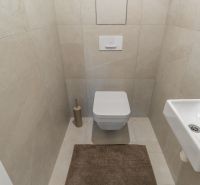 Hänge-WC, kleines Waschbecken und beigefarbene Fliesen im Badezimmer, Wohnungsbau.