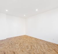 Ein Zimmer in einer 2-Zimmer-Wohnung mit weißen Wänden und einem Boden in Holzoptik.