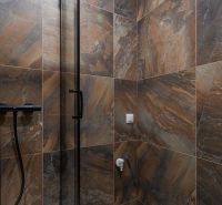 Badezimmer in einer 2-Zimmer-Wohnung mit dunklen Fliesen und einer Glas-Duschwand.