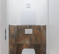 Toilette mit braunen Fliesen in einer 2-Zimmer-Wohnung.