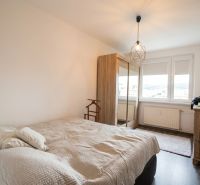 Helles Schlafzimmer mit Schrank, Bett und Boden mit Holzdekor in einer 2-Zimmer-Wohnung.