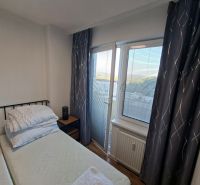 Schlafbereich in einer Einzimmerwohnung mit Vorhängen und einem Fenster mit Aussicht.