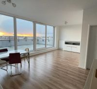 Wohnzimmer mit Esstisch, großen Fenstern und Holzboden.