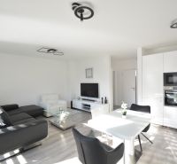 Wohnzimmer mit Küche, schwarzem Sofa und Holzboden in einer 3-Zimmer-Wohnung.