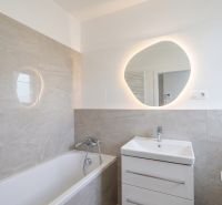 Badezimmer in einer 2-Zimmer-Wohnung mit Badewanne, Waschbecken und beleuchtetem Spiegel.