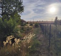 Sonnige Grundstücke in Jasová mit Rasenflächen und Bäumen, neben dem Zaun.