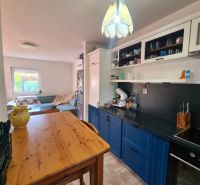 Eine Küche in einem Einfamilienhaus mit einem Holztisch, blauen Schränken und einem Sofa im Hintergrund.