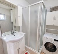 Badezimmer in einem Einfamilienhaus mit Waschbecken, Duschkabine und Waschmaschine.