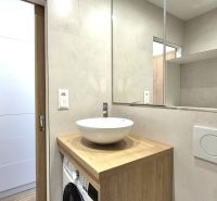 Badezimmer in einem Studio-Apartment mit weißem Waschbecken, Holzdekor und Aufbewahrungskörben.