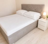 Bett mit Nachttisch und Lampe in einer 2-Zimmer-Wohnung auf einem Boden mit Holzdekor.