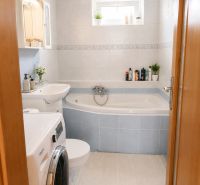 Badezimmer in einer 2-Zimmer-Wohnung mit Badewanne, Waschmaschine und Fliesen in hellem Farbton.