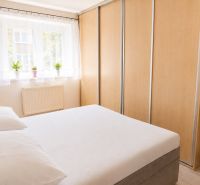 Schlafzimmer in einer 2-Zimmer-Wohnung mit Bett, Schränken und einem Fenster mit Pflanzen.