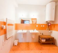 Badezimmer in einer 3-Zimmer-Wohnung mit orangefarbenen Fliesen, zwei Waschbecken und einem Boiler.