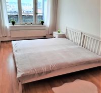Helles Schlafzimmer in einer Zweizimmerwohnung mit Fenster und Boden in Holzoptik.