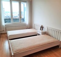 Schlafzimmer mit zwei Betten, einem Nachttisch und einem Boden mit Holzdekor in einer Zweizimmerwohnung.