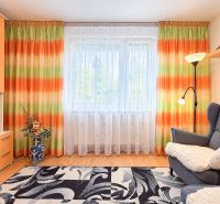 Bunte Vorhänge, Sessel und Stehlampe, Teppich mit geometrischem Muster in einer Einzimmerwohnung.