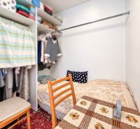 Ein Schlafzimmer mit Bett, Schrank und Stühlen in einer Einzimmerwohnung mit gemustertem Teppich.