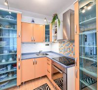 Küche in einer Einzimmerwohnung mit orangefarbenen Schränken, Glasvitrinen und Geräten.