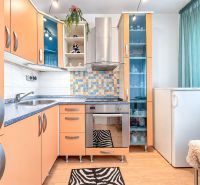 Küche in einer Einzimmerwohnung mit bunten Schränken, Fliesenmosaik und Bodenbelag in Holzoptik.