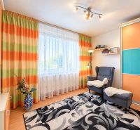 Wohnzimmer in einer Einzimmerwohnung mit bunten Vorhängen und einem Sessel auf einem Boden mit Holzdekor.