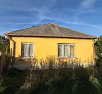 Gelbes Einfamilienhaus in Komárno mit Zaun und Garten unter blauem Himmel.