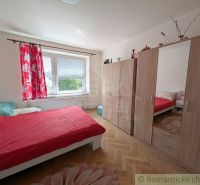 Schlafzimmer mit roter Bettwäsche, einem Schrank und einem Boden mit Holzdekor in einer 2-Zimmer-Wohnung.
