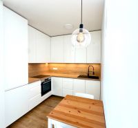 Küche in einer 2-Zimmer-Wohnung mit weißen Schränken, Holzdekor und Hängelampen.