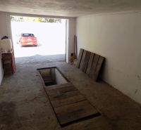 Garage mit Wartungsgrube, älterer Betonboden und geparktes Auto draußen.