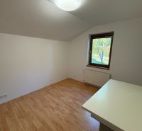 Ein Zimmer mit einem Boden in Holzoptik, einem Tisch und einem Fenster in einem Einfamilienhaus.