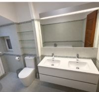 Badezimmer in einem Einfamilienhaus mit Doppelwaschbecken, WC und Spiegel.